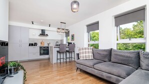 A modern kitchen with grey cabinets, a dining area with a grey sofa, and large windows with a view of greenery. - Spacious 2BR - Parking Near Edinburgh City Centre (Edinburgh)