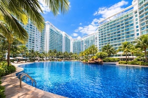 A large swimming pool surrounded by palm trees and hotel buildings.
