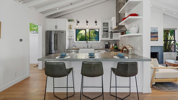 A modern kitchen with a central island, bar stools, and a view of greenery outside. - Humphrey House | Walk to Beach, Coast Village Rd, 3 En Suite Bedrooms (Montecito)