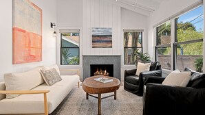 A living room with a fireplace, a sofa, a coffee table, and a view of the outside. - Humphrey House | Walk to Beach, Coast Village Rd, 3 En Suite Bedrooms (Montecito)