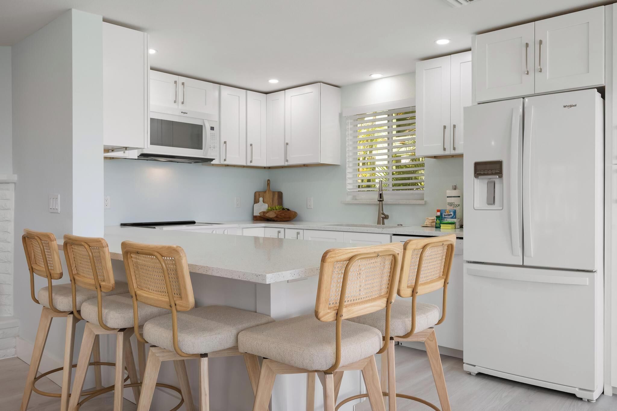 A modern kitchen with white cabinetry, a central island with bar stools, a built-in microwave, and a refrigerator.