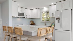 A modern kitchen with white cabinetry, a central island with bar stools, a built-in microwave, and a refrigerator. - Manatee Cove -3-bedroom bayfront home with dock (Bradenton Beach)