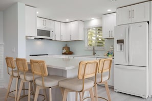 Una cocina moderna con armarios blancos, una isla central con taburetes, un microondas integrado y un refrigerador.