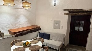Tunnelmallinen huone, jossa on kivilaattalattia, pyöreä pöytä, jonka päällä on punotut alustat, rottinkituolit, tyynyillä varustettu penkki ja puinen hylly.