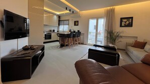 Una sala de estar moderna con un televisor de pantalla plana, un sofá, una mesa de centro y una cocina al fondo.