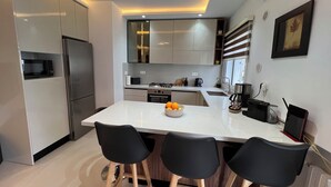 Una cocina moderna con encimera blanca, electrodomésticos de acero inoxidable y sillas negras.