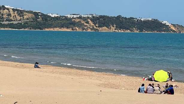 Una playa con gente, un paraguas amarillo y edificios en una colina al fondo.