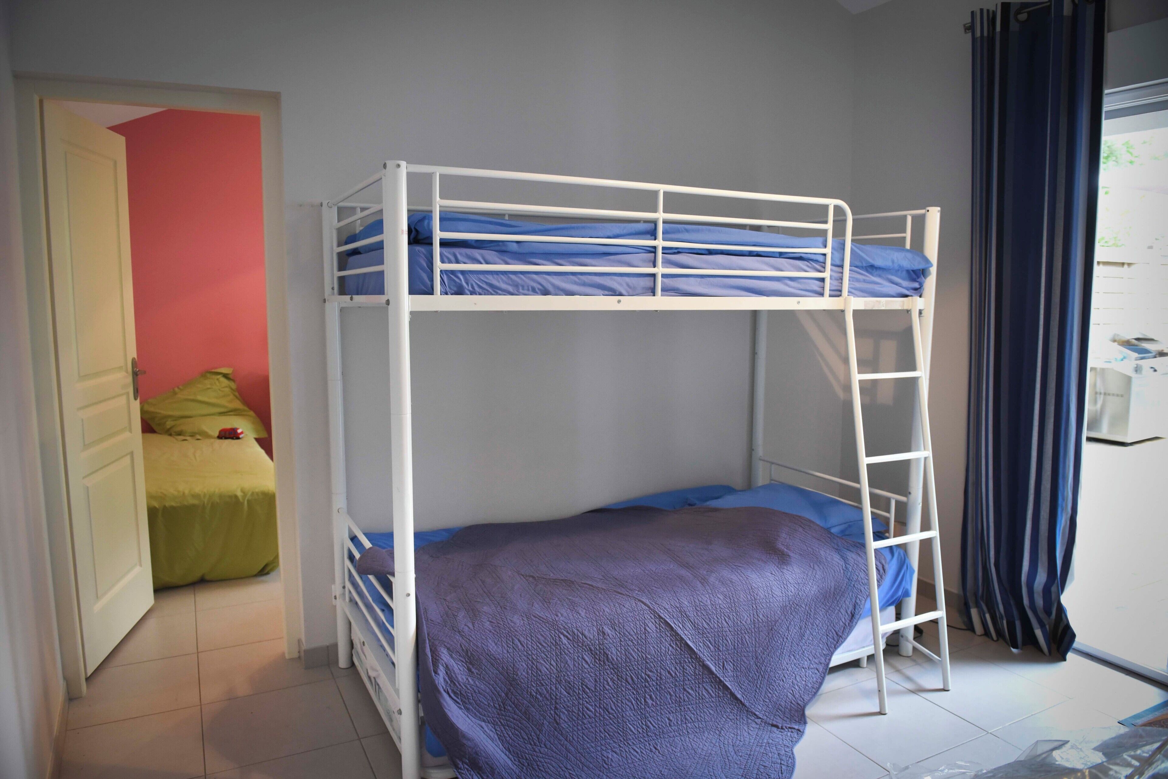 Una cama litera con escalera, una puerta que da a otra habitación y una ventana con cortinas.