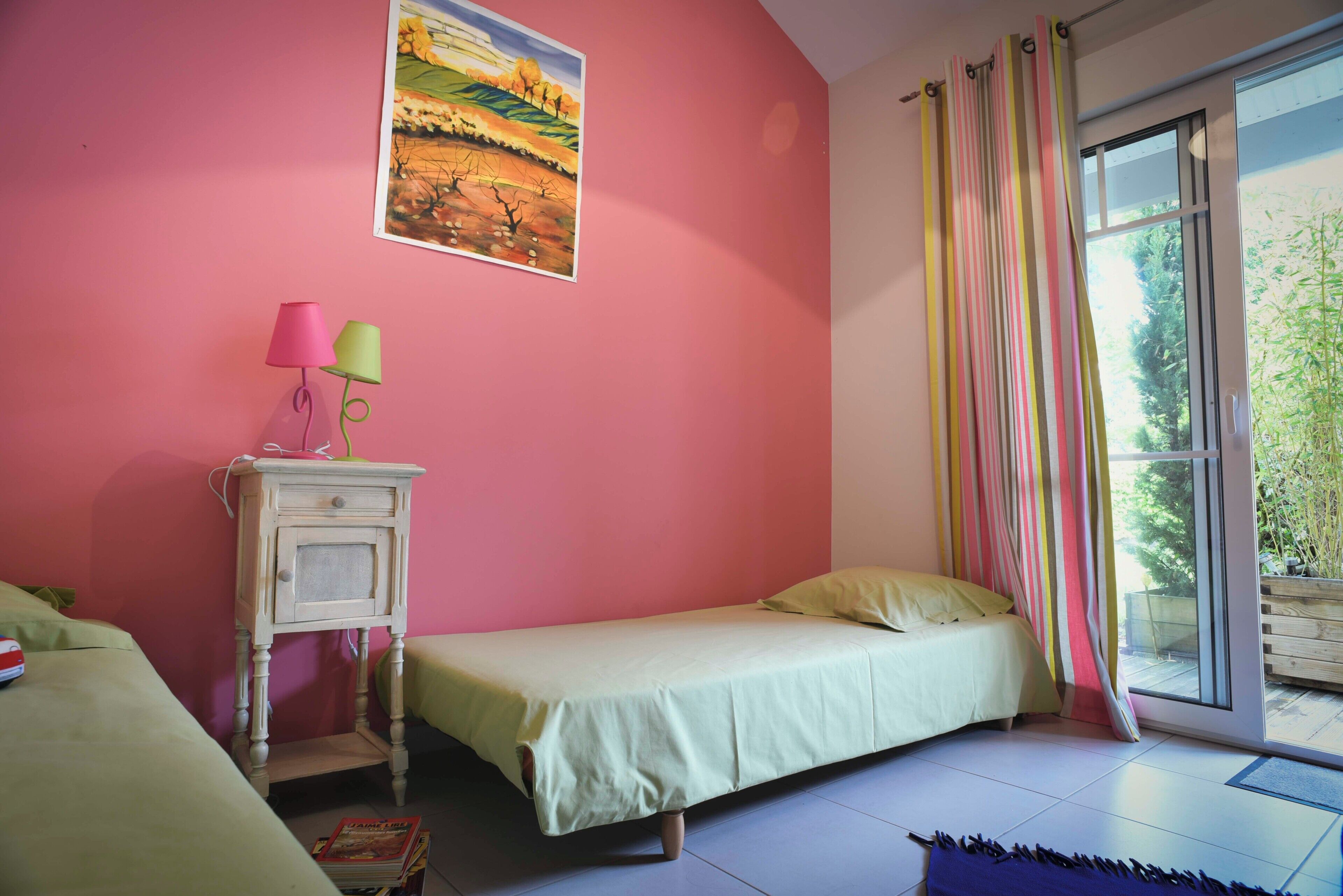 A room with a bed, a nightstand with lamps, a painting, and a window with curtains.