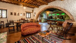 A rustic interior with a wooden ceiling, a patterned sofa, a dining area, and a kitchen visible through an archway.