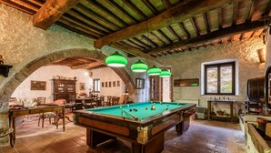 A billiards room with a pool table, wooden furniture, and green pendant lights.