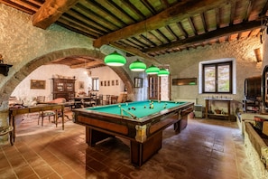 Una sala biliardo con tavolo da biliardo, arredi in legno e lampade a sospensione verdi.