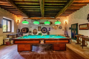 Un tavolo da biliardo in una stanza rustica con travi in legno, una finestra e diverse decorazioni alle pareti.