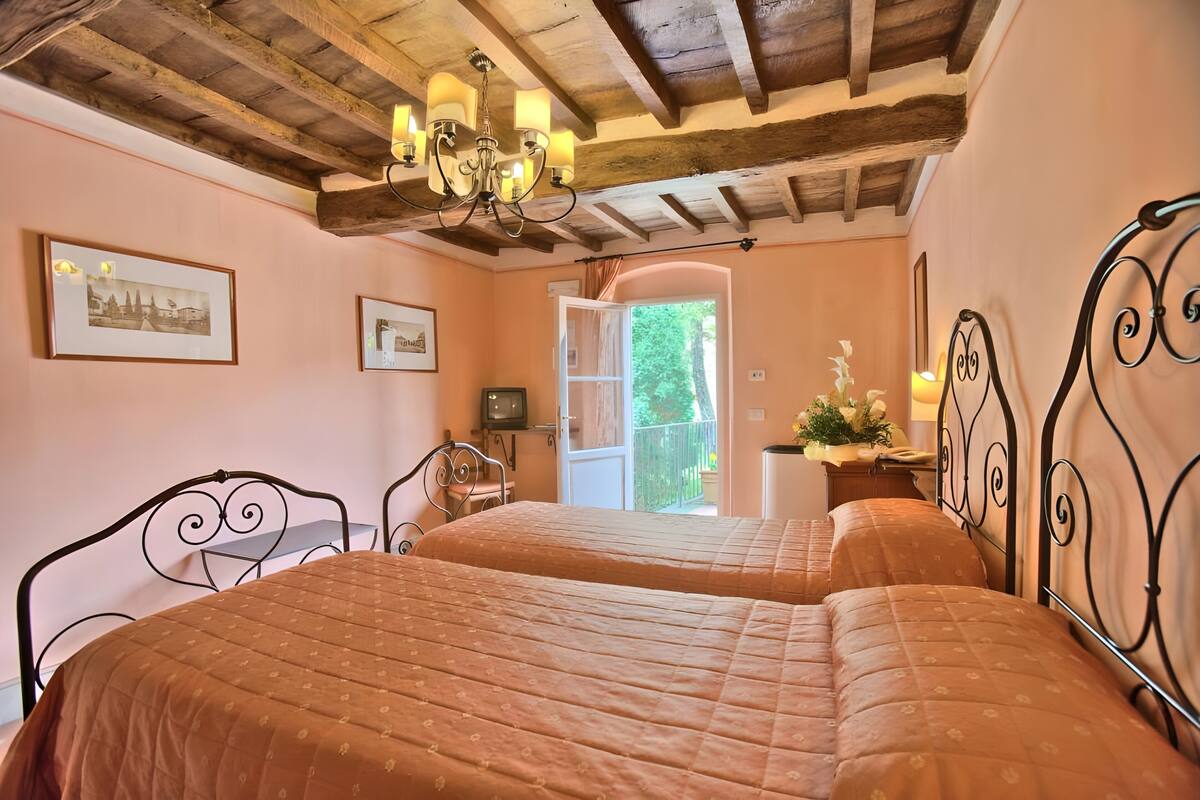 Un dormitorio con dos camas, una araña, cuadros enmarcados y vistas al exterior.