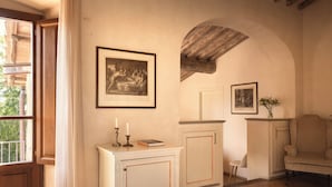 A room with a wooden door, a white cabinet with a book and candles, and two framed pictures on the wall. - Villa Barberino (Meleto)