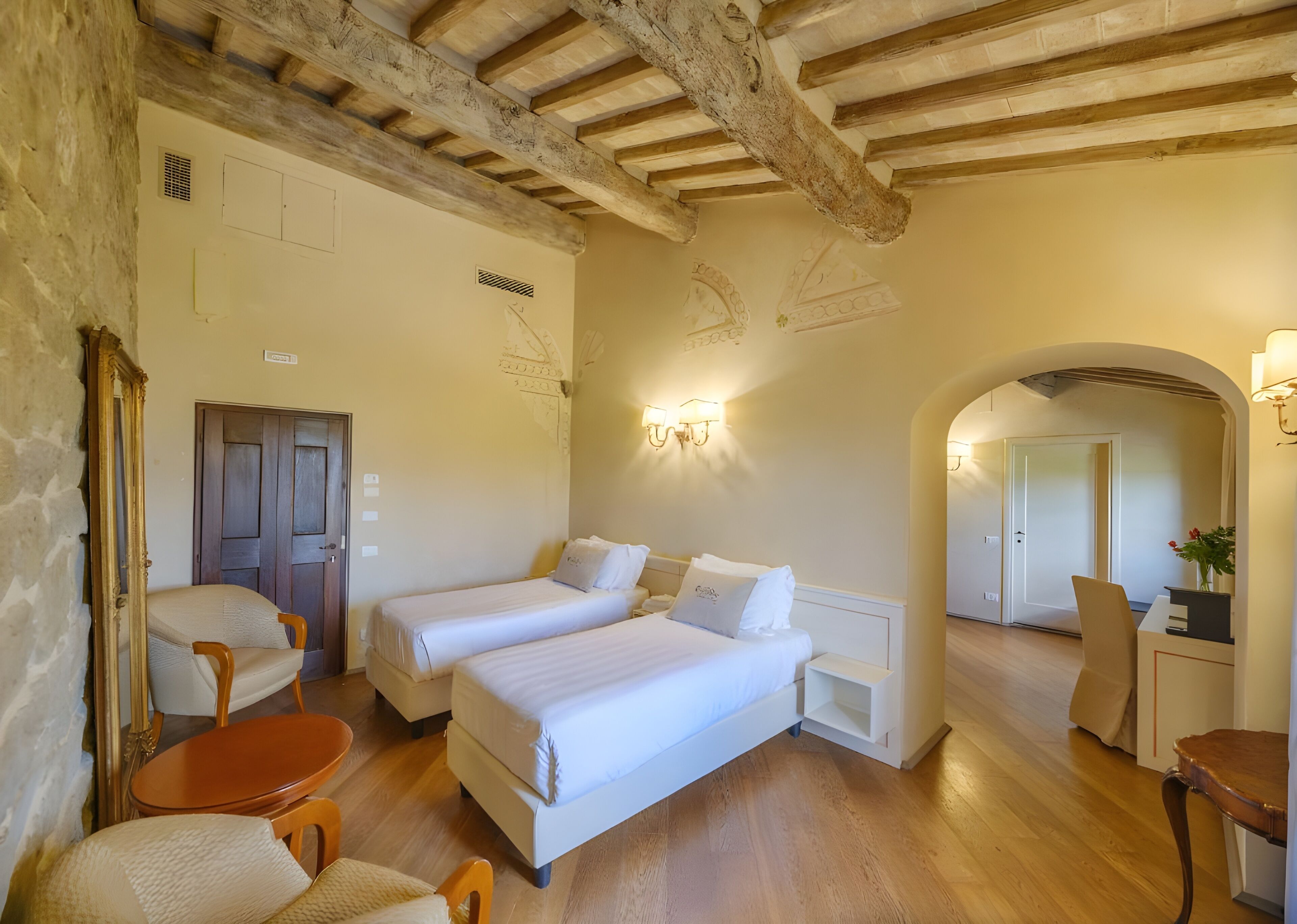 Una habitación con dos camas, piso de madera, un escritorio con silla y un espejo.