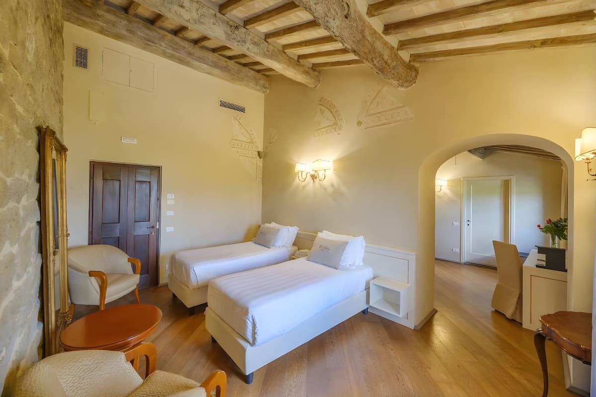 Una habitación con dos camas, piso de madera, un escritorio con silla y un espejo.