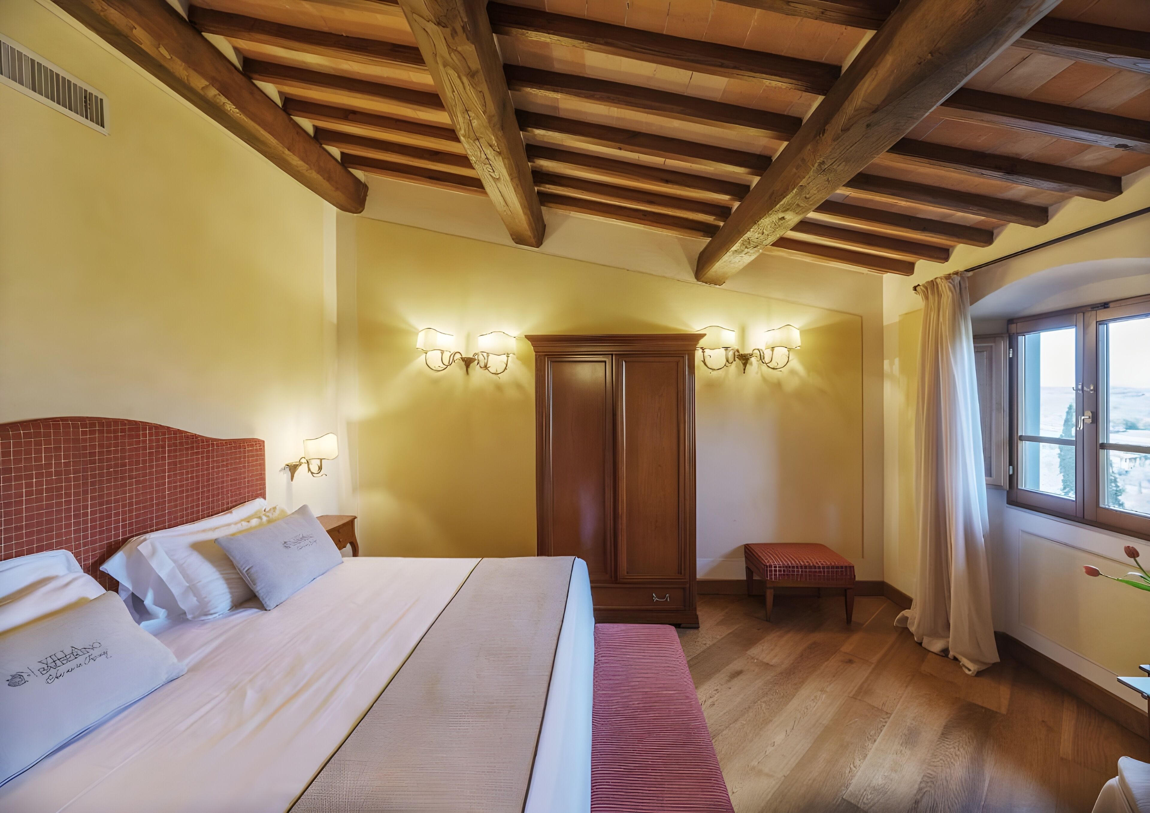 Una habitación de hotel con techo de madera, una cama grande, un armario y una ventana con cortinas.