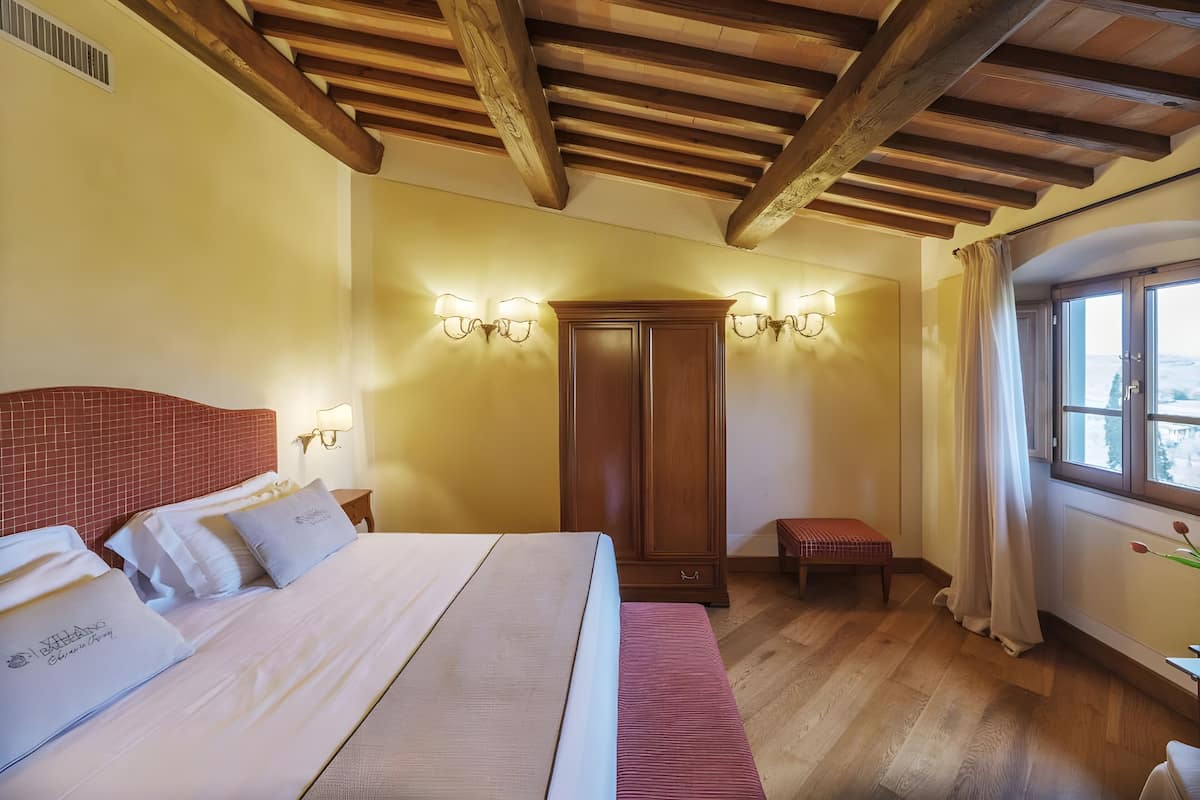 Una habitación de hotel con techo de madera, una cama grande, un armario y una ventana con cortinas.