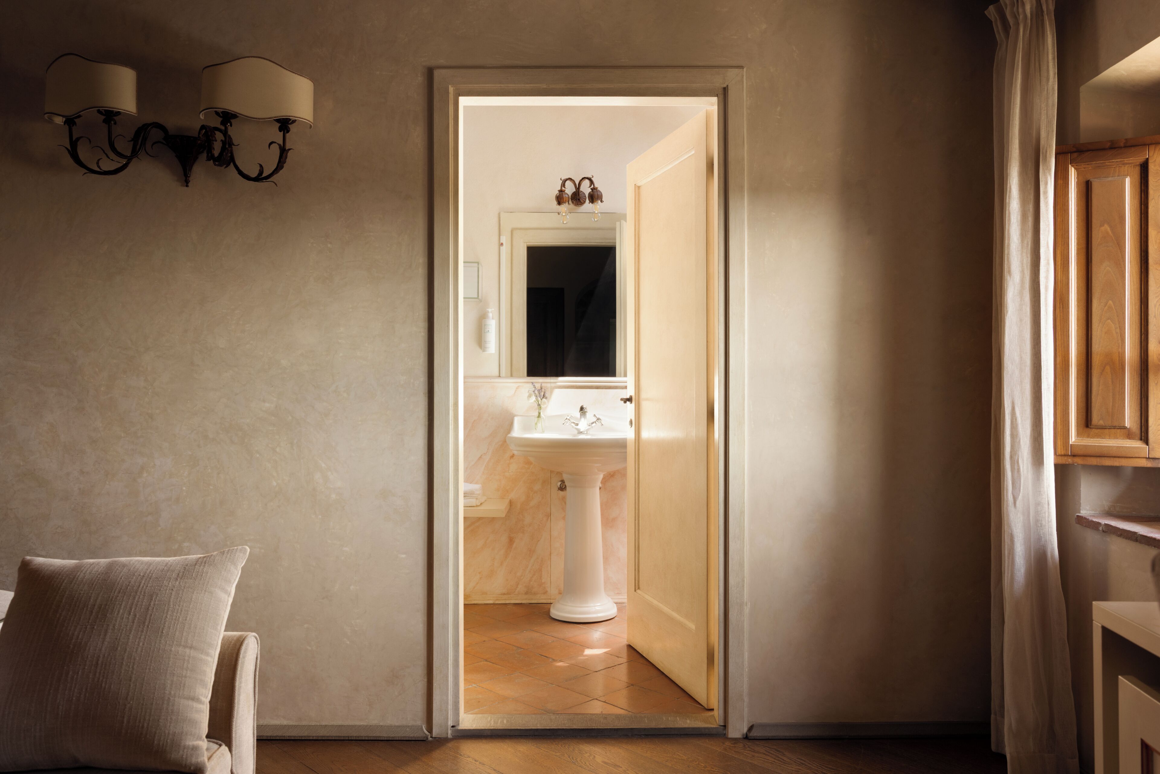 Un baño con un lavamanos pedestal blanco, un espejo encima y un perchero en la pared.