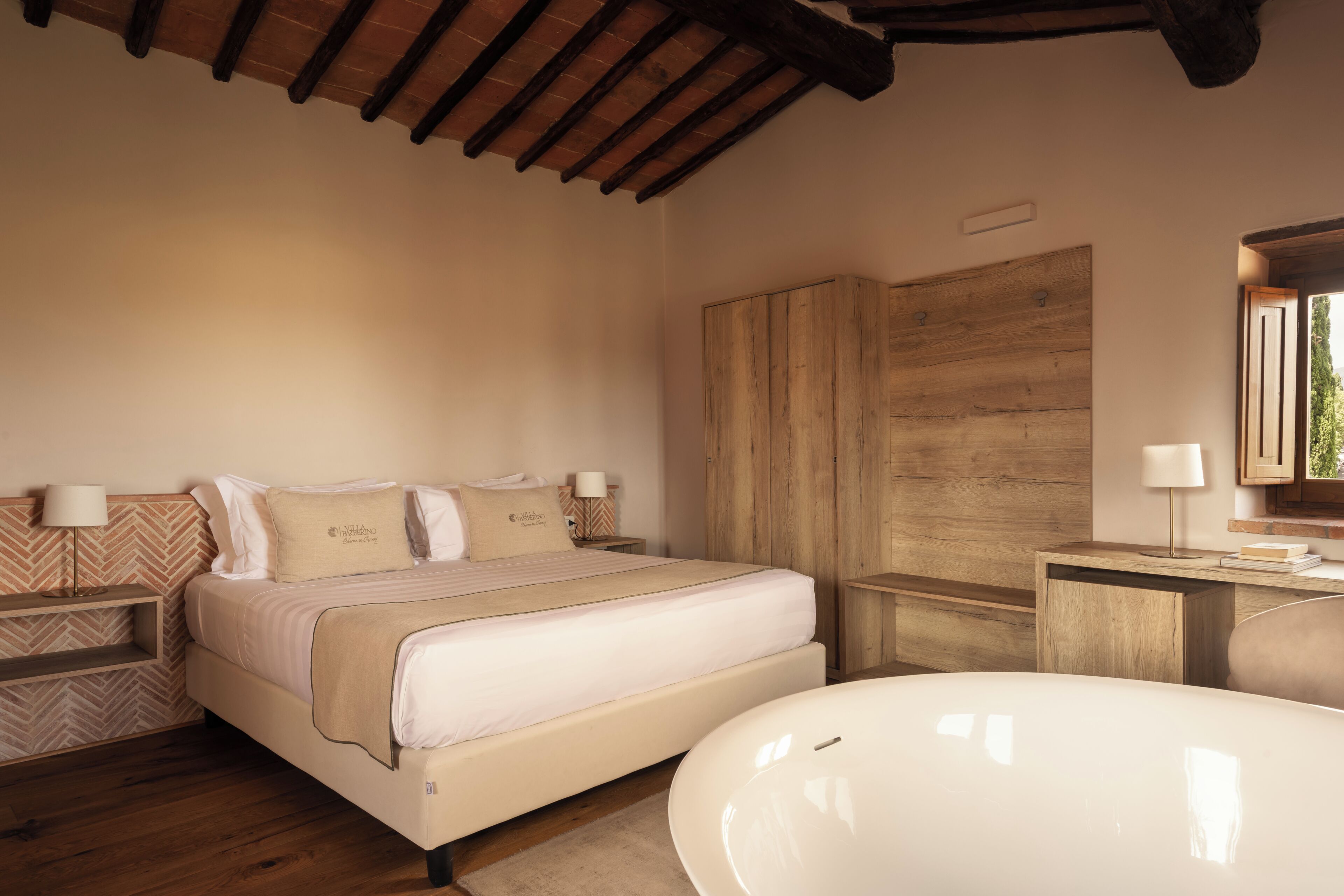 Ein Schlafzimmer mit einem Bett, Nachttischen, einem großen Holzschrank, einem Badezimmer mit einer Badewanne und einem Fenster mit Blick.