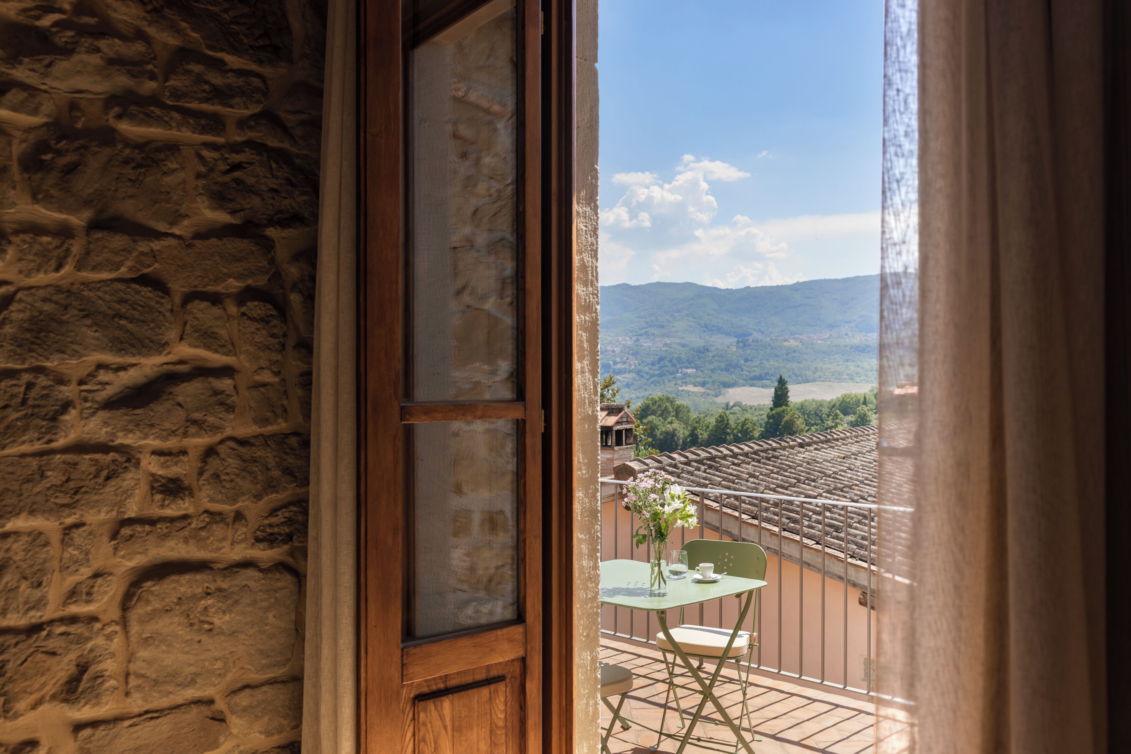Ein Balkon mit Tisch und Stühlen, einem Blumenstrauß und Blick auf eine gebirgige Landschaft.