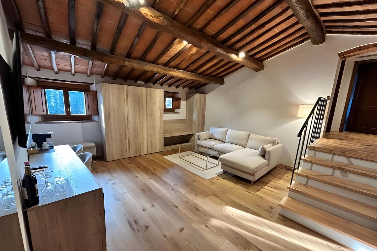 Una habitación estilo loft con techo de madera, un sofá blanco, una mesa de comedor y una escalera.