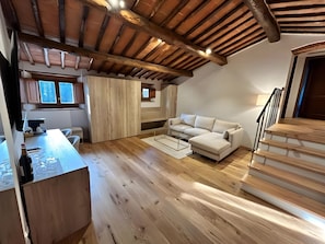 Una habitación estilo loft con techo de madera, un sofá blanco, una mesa de comedor y una escalera.