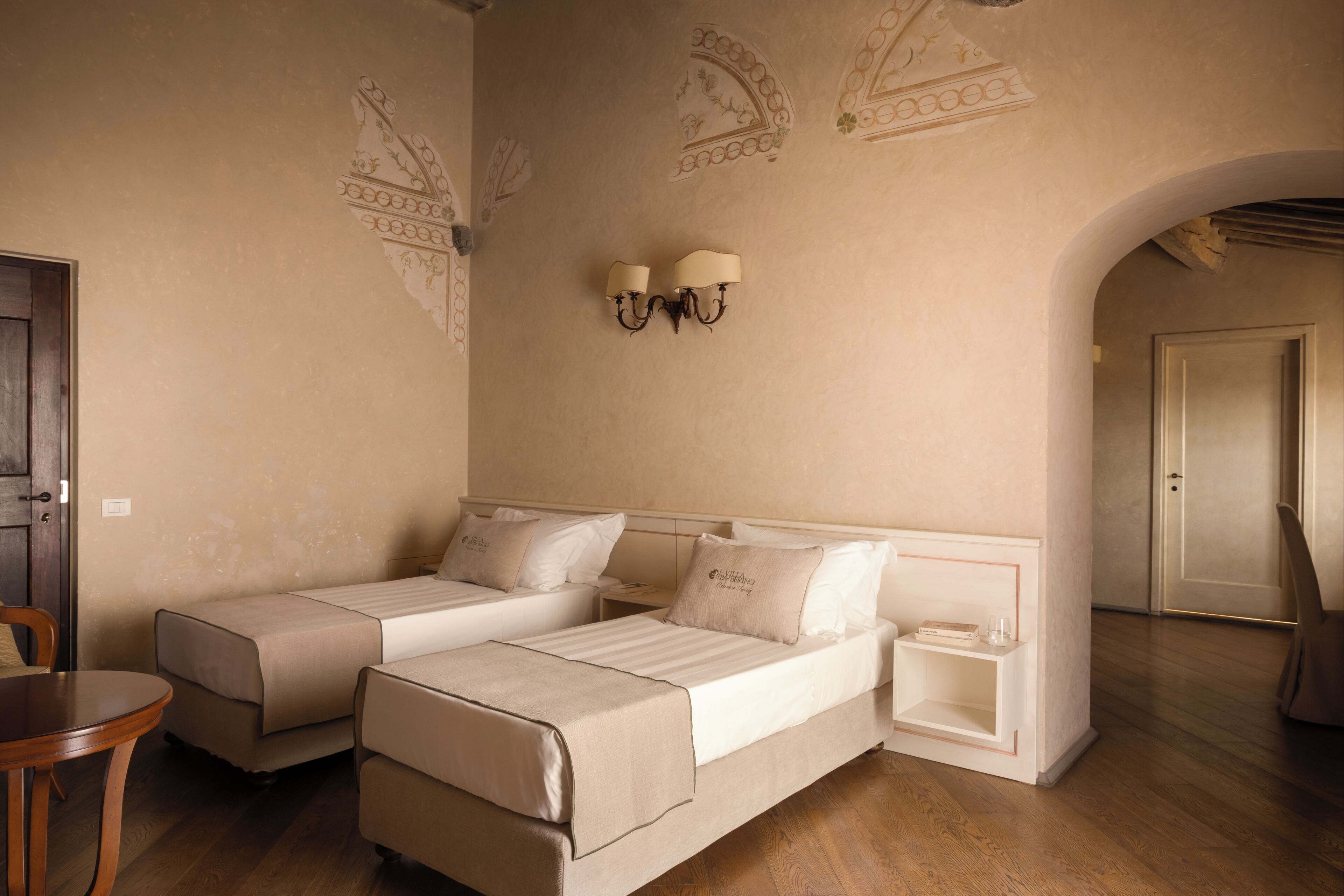 A room with two beds, a wooden floor, and a wall with decorative patterns.