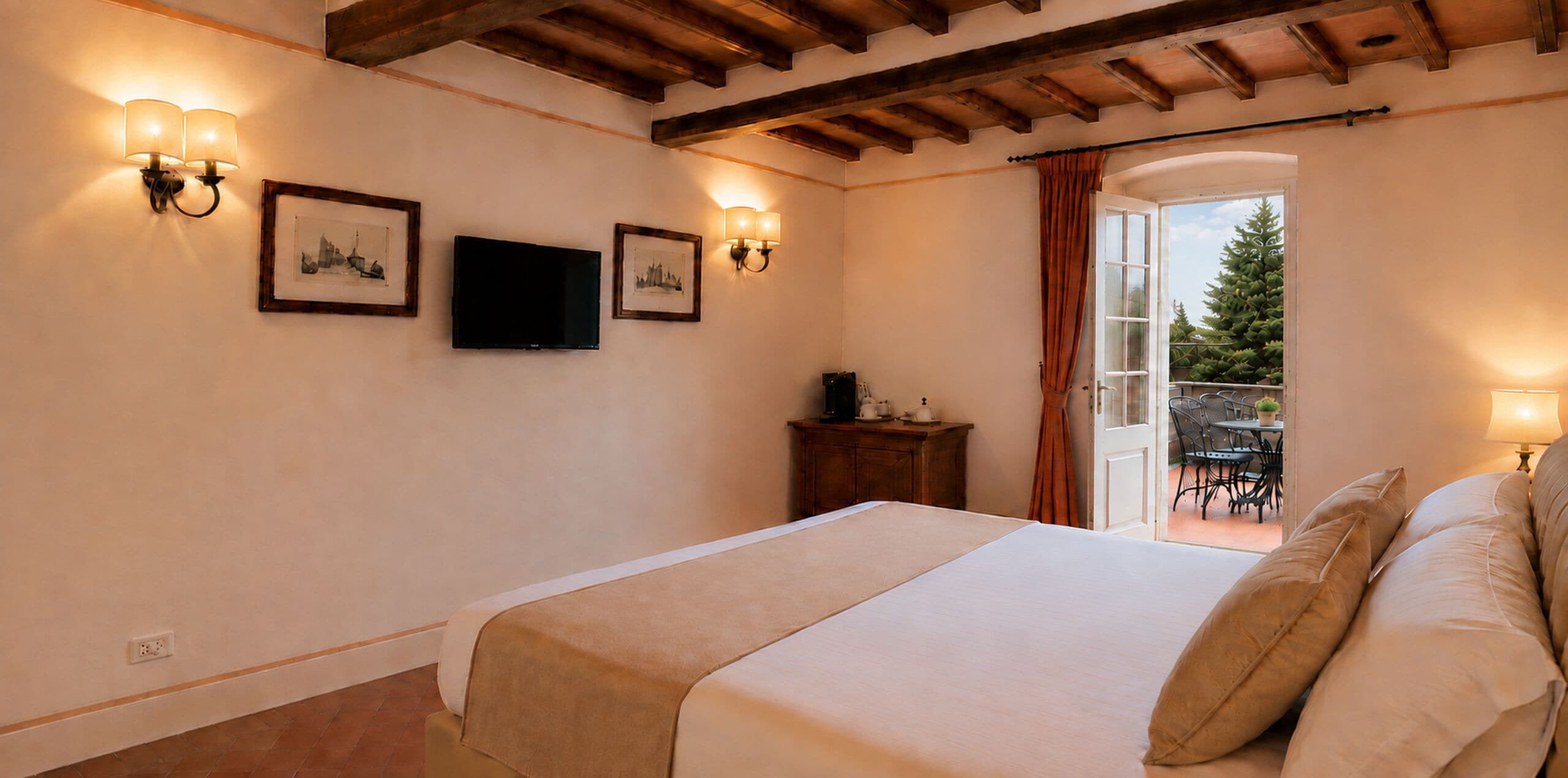 A bedroom with a bed, a television, wall-mounted lights, and a view of an outdoor area with a table and chairs.