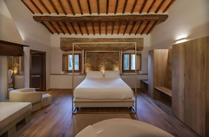 Un dormitorio con cama con dosel, vigas de madera en el techo, pared de piedra y vistas a árboles a través de las ventanas.