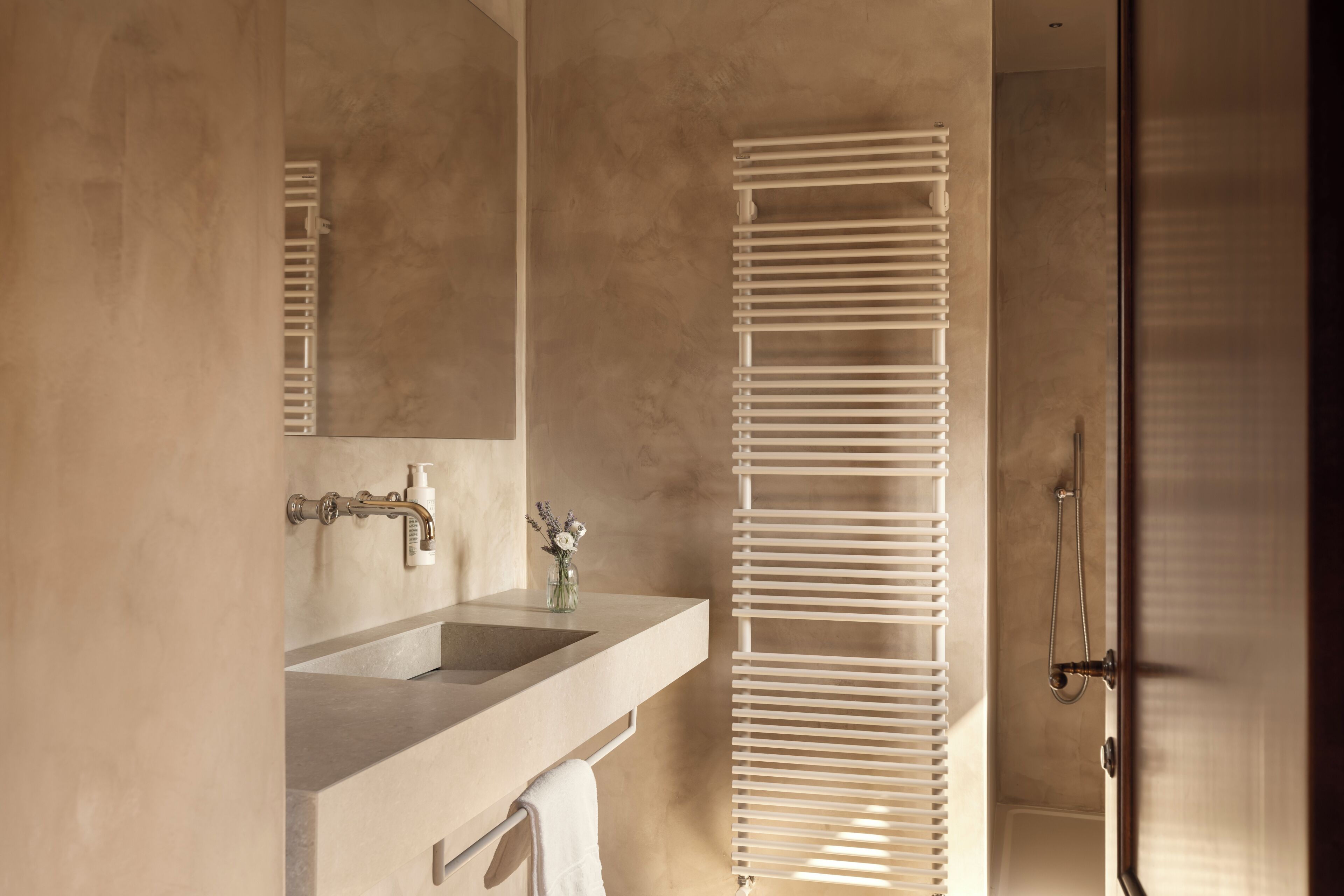 A bathroom with a sink, mirror, towel rack, and a shower area.