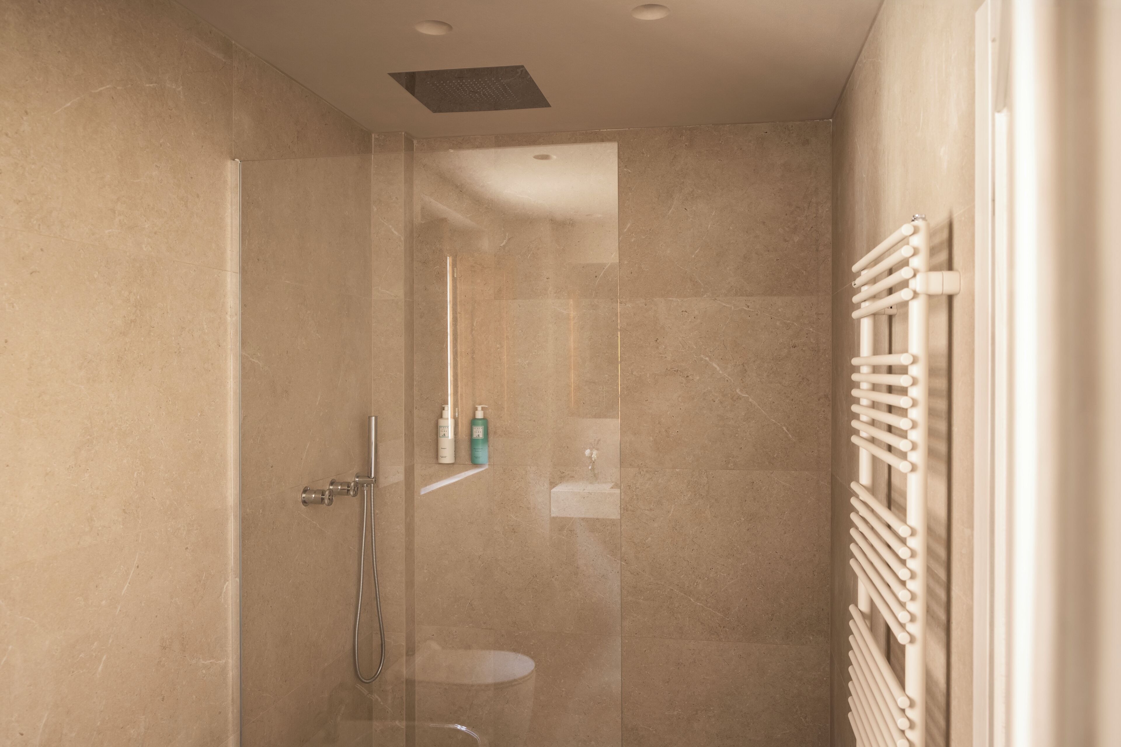 Une douche moderne dotée d’une porte en verre, d’un pommeau de douche à main et d’un porte-serviettes fixé au mur.