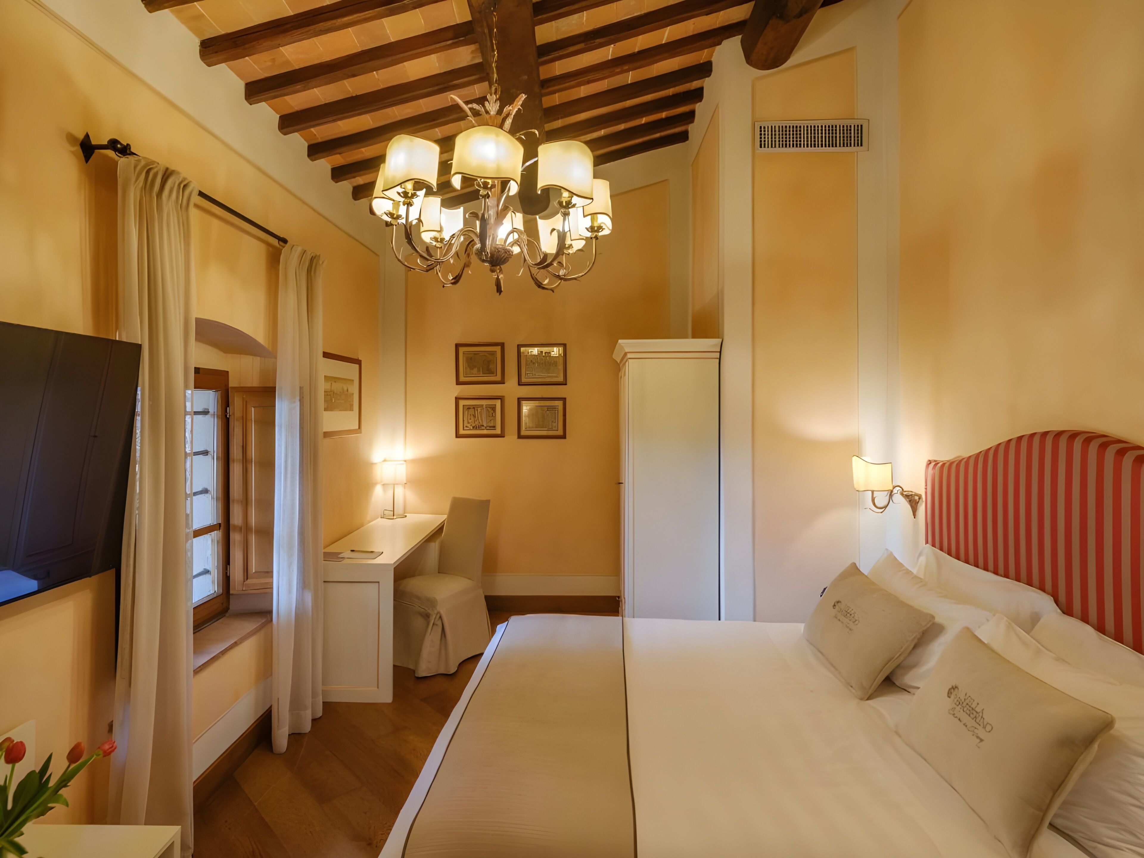 Una habitación de hotel con cama, escritorio, silla, televisión y candelabro.