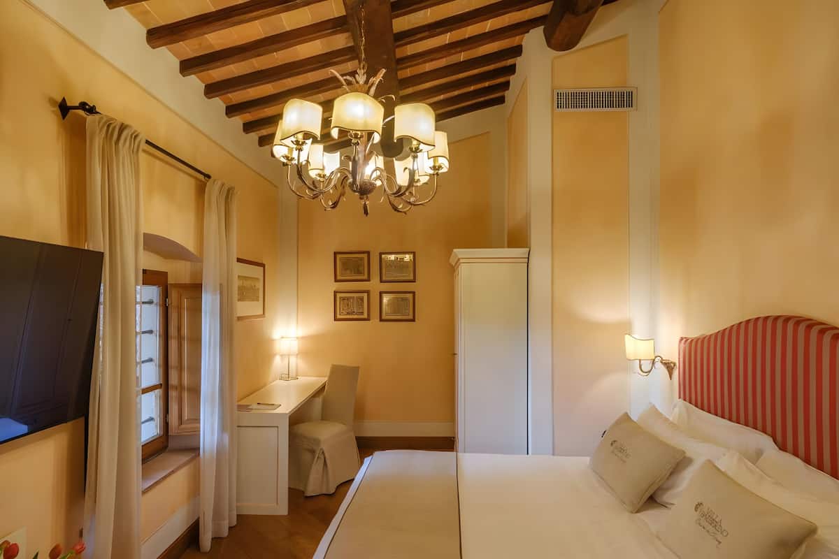 Una habitación de hotel con cama, escritorio, silla, televisión y candelabro.