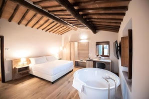 A bedroom with a bed, bedside table, lamp, and a large bathtub.