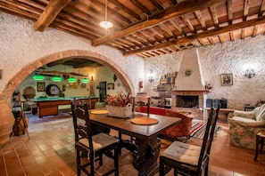 Un interno rustico con un tavolo da biliardo, sedie di legno, un camino e un muro in pietra.