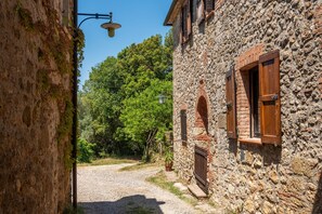 Una stretta strada acciottolata con edifici in pietra, un vialetto sterrato e un cielo azzurro limpido.