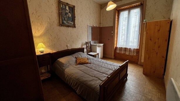 Ein Schlafzimmer mit Bett, Nachttisch, Lampe, Spiegel, Fenster mit Vorhängen und einem Holzschrank.