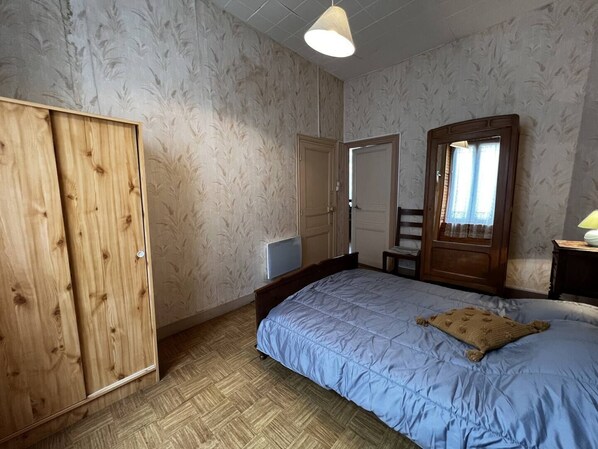 A bedroom with a bed, wooden wardrobe, a chair, and a window with curtains.