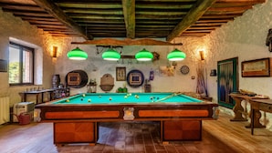 Een pooltafel in een rustieke kamer met houten balken, een raam en diverse wanddecoraties.