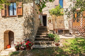 A stone building with a wooden door, a staircase leading to a door, and potted plants. - Brunello Apartment at Ritiro del Podestà Murlo (Murlo)
