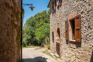 Una stretta strada acciottolata con edifici in pietra, un vialetto sterrato e un cielo azzurro limpido.