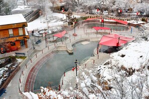 A snow-covered outdoor pool area with red canopies, a stone pathway, and a building with a red roof. - Lava Landing – Spacious In-Town Retreat (Lava Hot Springs)