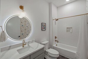 Kylpyhuone, jossa on pyöreä peili, pesuallas, wc-istuin ja kylpyamme.