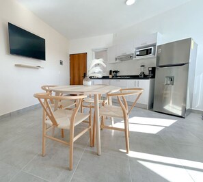 A modern kitchen with white cabinets, a stainless steel refrigerator, a microwave, and a dining area with a round table and wooden chairs. - Estancia Cómoda en Centro Vallarta - 1 (Puerto Vallarta)