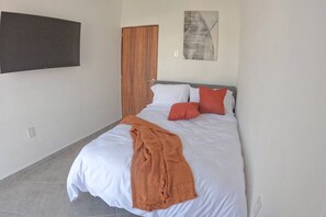 A bedroom with a bed, a television mounted on the wall, a door, and a painting. - Estancia Cómoda en Centro Vallarta - 1 (Puerto Vallarta)
