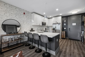 Une cuisine moderne avec des meubles blancs, un îlot central doté de tabourets de bar, un miroir rond et une enseigne portant l’inscription « Happy House ».