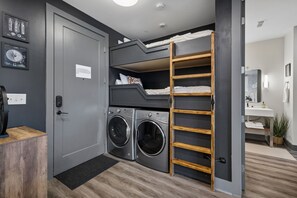 A compact laundry room with built-in washers and dryers, a wooden ladder, and a gray door. - Music City Condo・Mins to Broadway W Rooftop Lounge (Nashville)