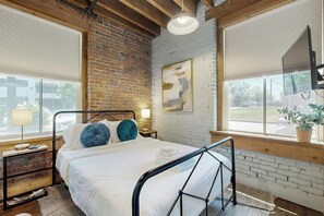 A room with a bed, a window, a brick wall, and a painting. - Luxe, historical condo home near downtown with WD, pool, outdoor lounge & grill (Nashville)